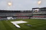 Ground crews work on the covers as rain falls at the MCG