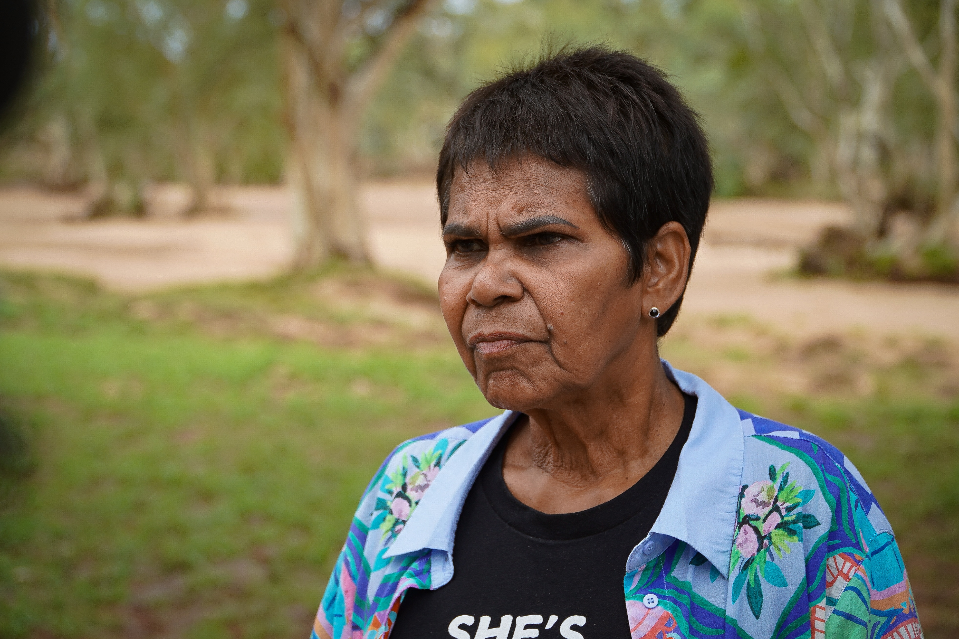 Uma mulher de cabelos curtos, com blusa azul sobre camisa preta, olha para a esquerda.