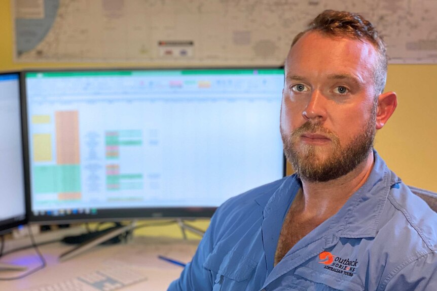 A head and shoulders shot of a bearded man sitting in front of a computer monitor.