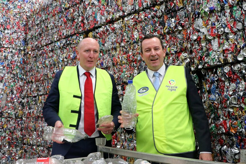 Mark McGowan and Mr Dawson hold up empty bottles in front of a giant pile of crushed cans.