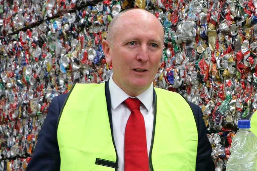 A mid shot of WA Environment Minister Stephen Dawson in front of a giant pile of recycling wearing a hi-vis vest.