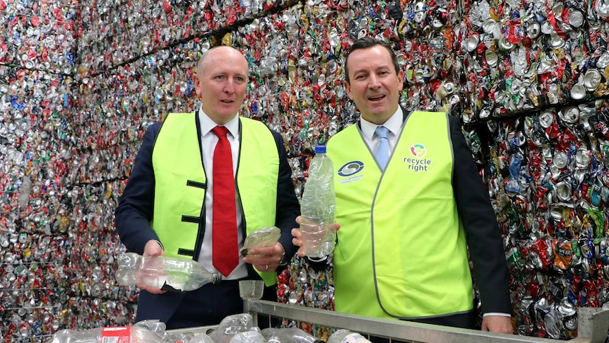 Mark McGowan and Mr Dawson hold up empty bottles in front of a giant pile of crushed cans.