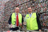 Mark McGowan and Mr Dawson hold up empty bottles in front of a giant pile of crushed cans.