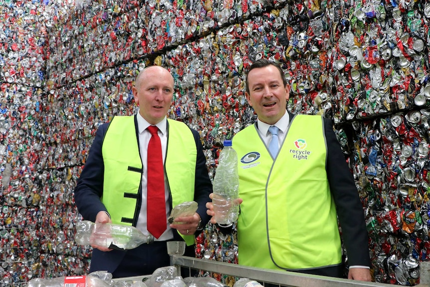 Mark McGowan and Mr Dawson hold up empty bottles in front of a giant pile of crushed cans.