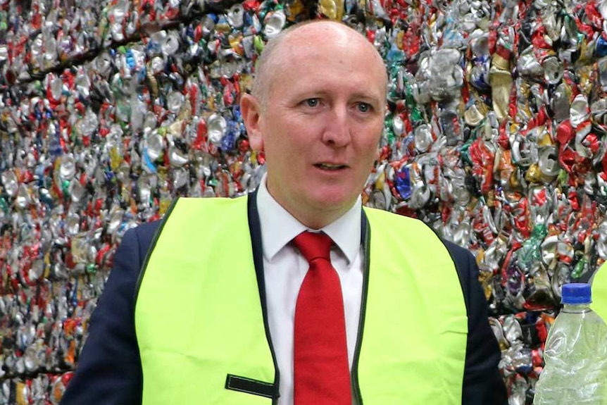 Mark McGowan and Mr Dawson hold up empty bottles in front of a giant pile of crushed cans.