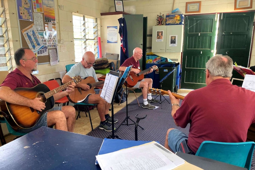 three men sit in a line playing guitar in a music workshop.