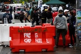 People walk past a barricade that reads' Welcome 2 'Free Cap Hill' spray painted on it in white and green