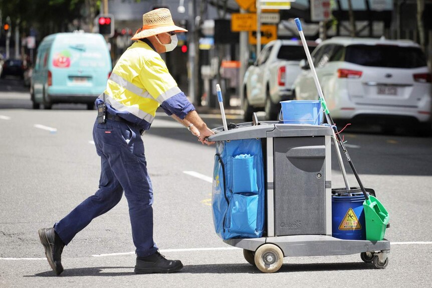 El trabajador de limpieza del consejo con una máscara que empuja un carrito cruza George Street en la ciudad de Brisbane el 11 de enero de 2021.