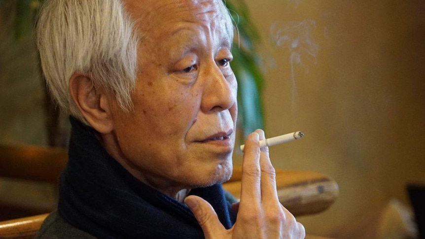 A man holds a cigarette to his lips as he sits in a restaurant.