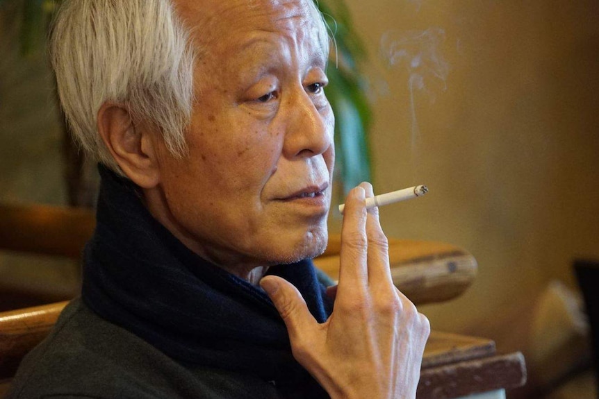 A man holds a cigarette to his lips as he sits in a restaurant.