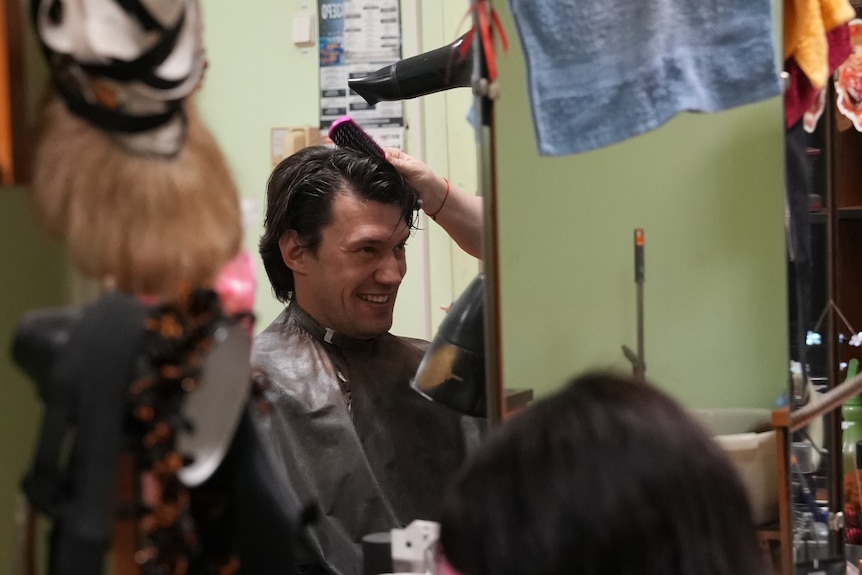 A man sitting in a chair while a person styles his hair