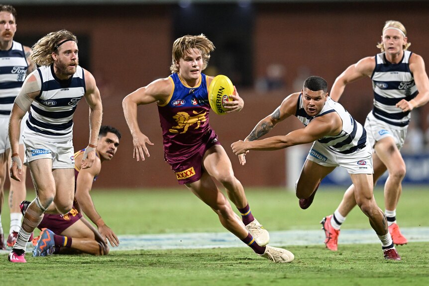 A Brisbane Lions player's runs with the ball in one arm as a Geelong defender reaches in vain to try and stop him.
