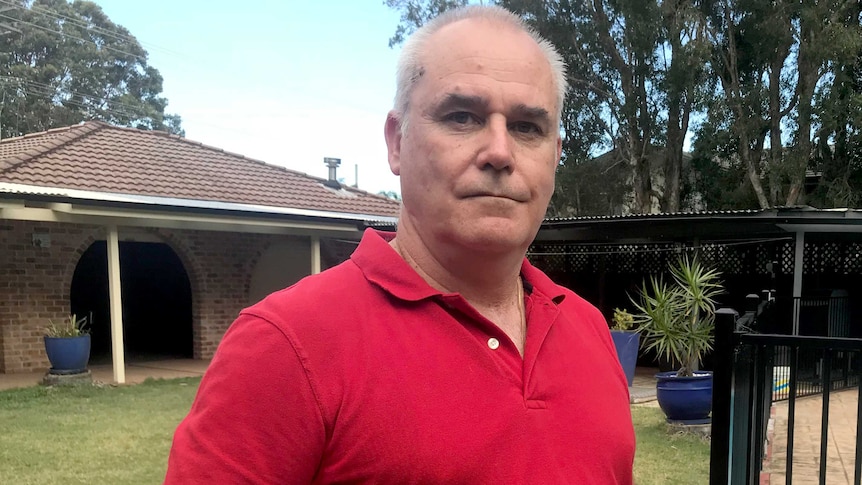 Peter stands in a backyard next to a pool fence with a single-storey brick and tile home visible behind him.