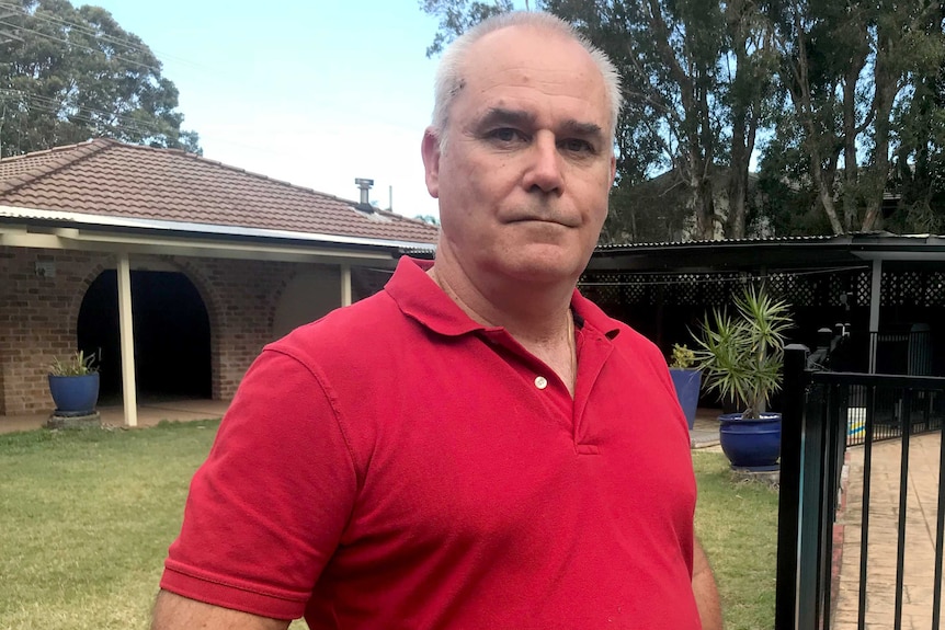 Peter stands in a backyard next to a pool fence with a single-storey brick and tile home visible behind him.