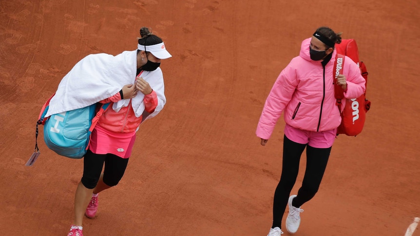 Victoria Azarenka (right) and Danka Kovinic are dressed warmly while walking on clay court at the French Open.