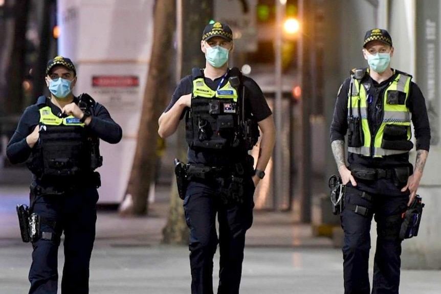 Three protective service officers wearing masks walk down a footpath in Melbourne's CBD.