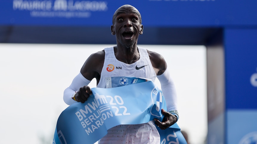 A man is pictured finishing a marathon in Berlin, his expression looks shocked and happy.