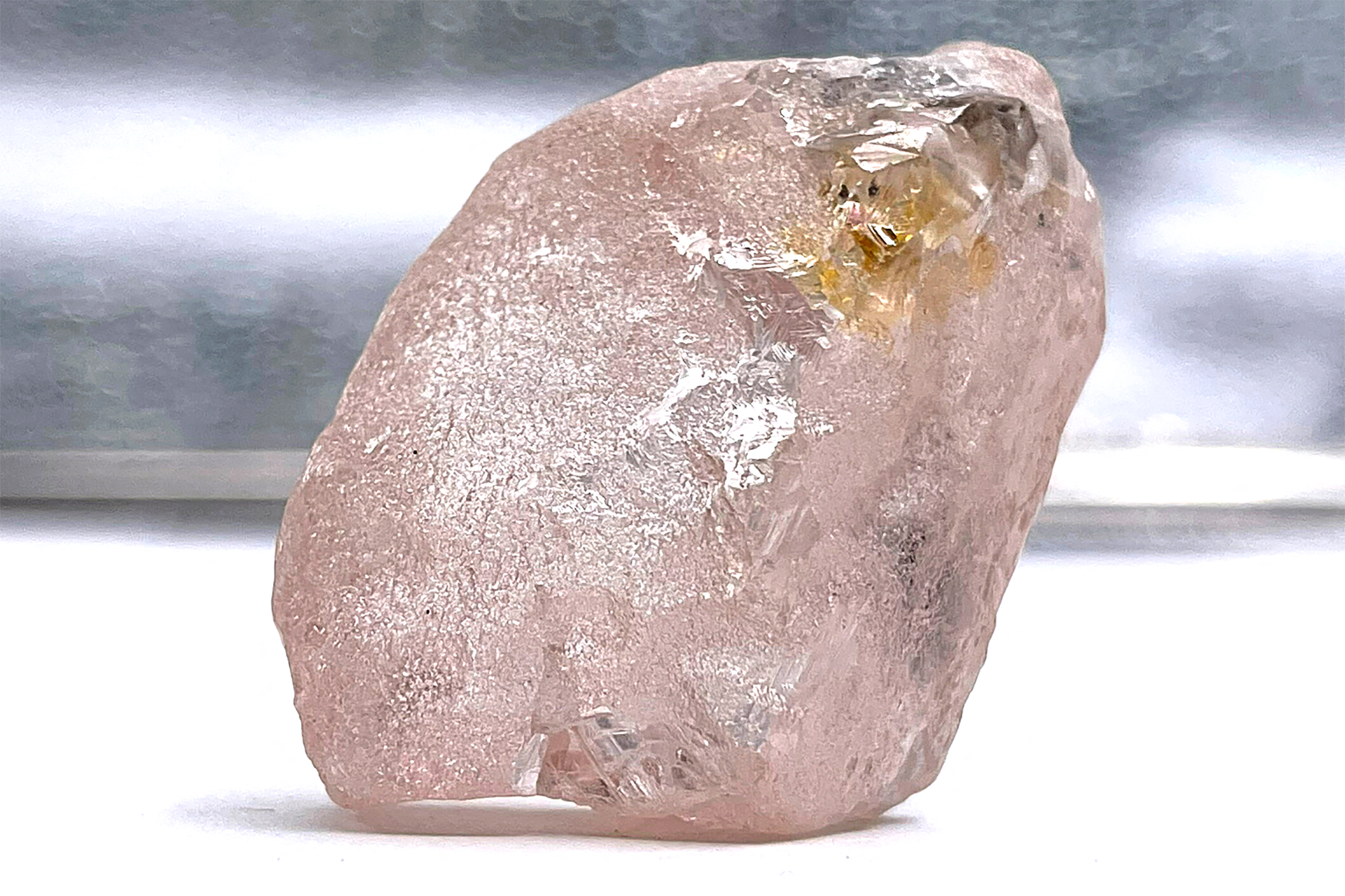 A large uncut, pink diamond sits on a table