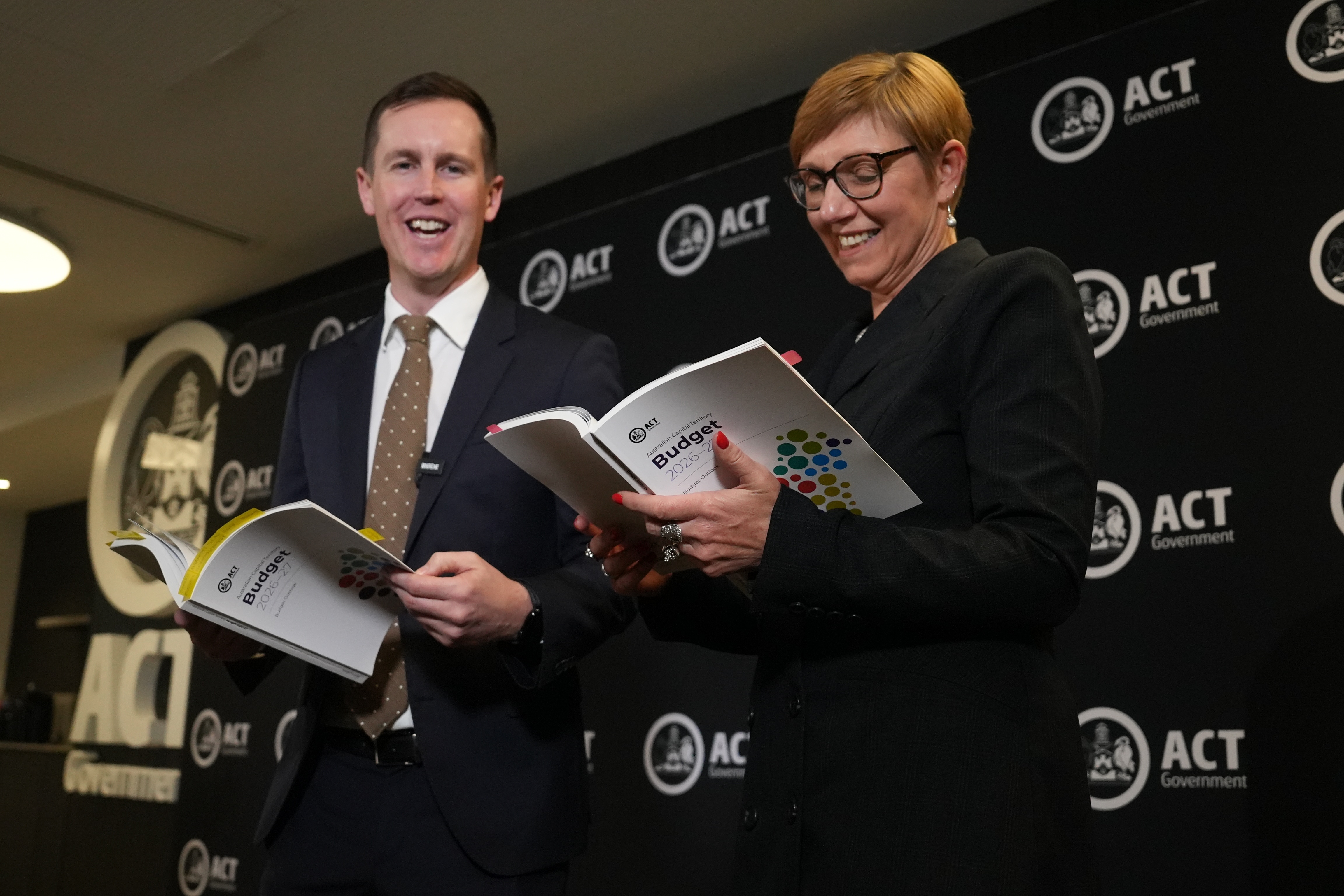A man and woman in suits hold budget papers while smiling.