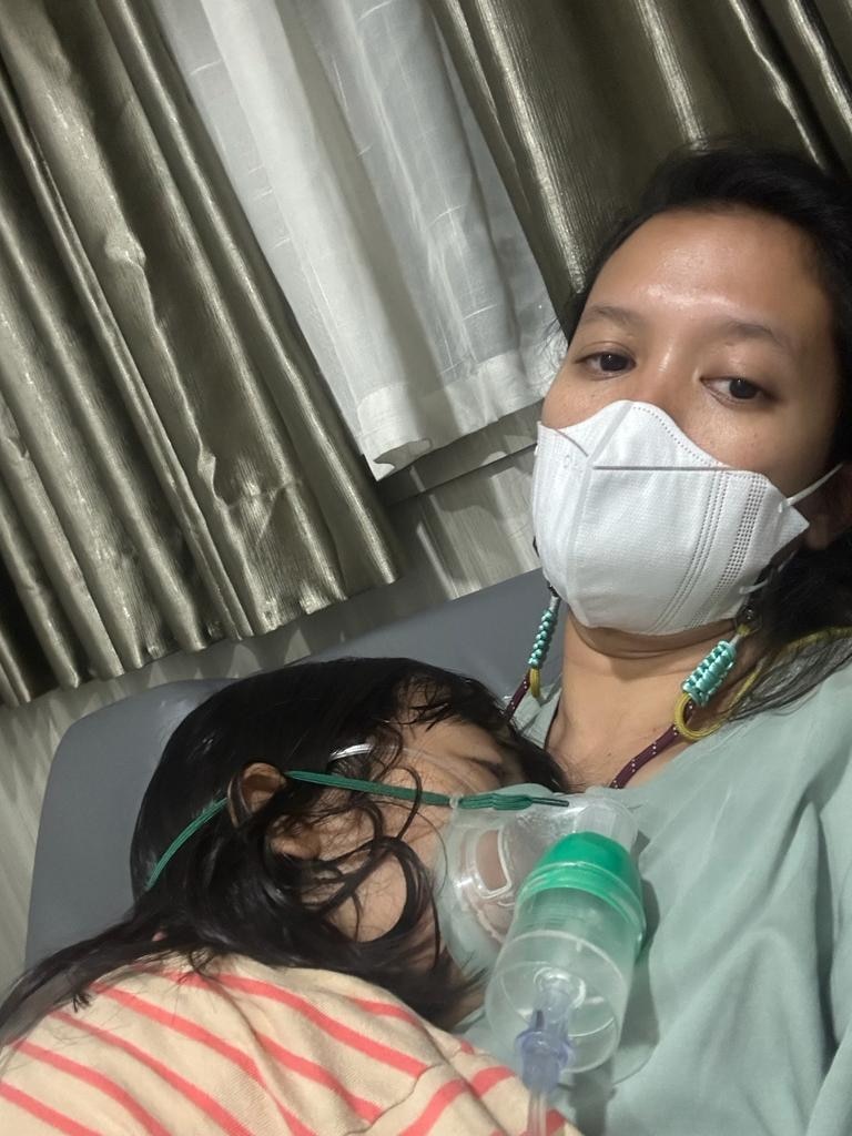 A little girl, with an oxygen mask over her nose and mouth, sleeps on her mother's chest.