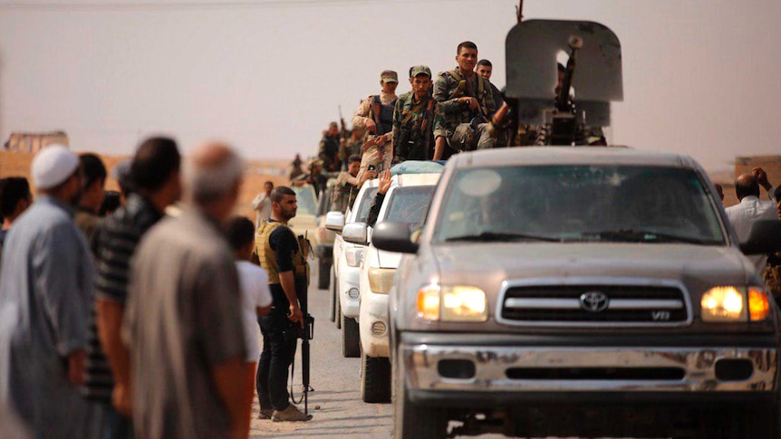 Syrian troops enter the town of Ein Issa in a convey of trucks as civilians stand on the road side.