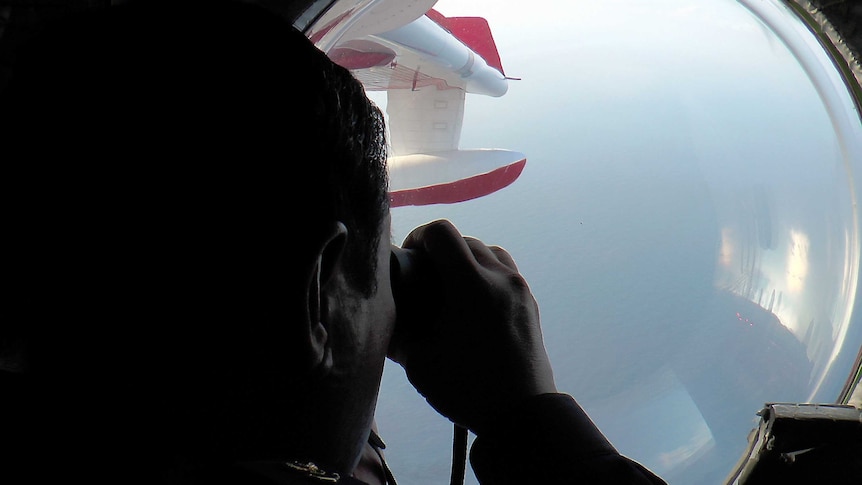 Malaysian Maritime Enforcement officer looks through binoculars while flying over waters searching for missing plane
