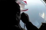 Malaysian Maritime Enforcement officer looks through binoculars while flying over waters searching for missing plane