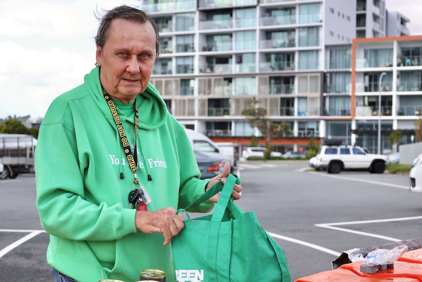 A man in a hoodie standing with a Woolworths bag.