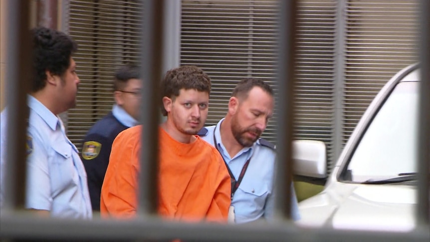 A man in orange is led away in handcuffs