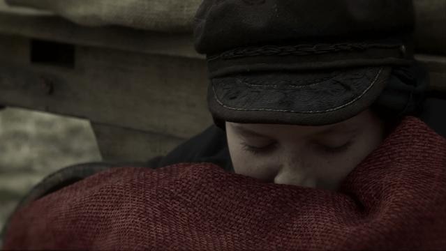 Girl in hat wrapped in rug as though she is cold and sleeping