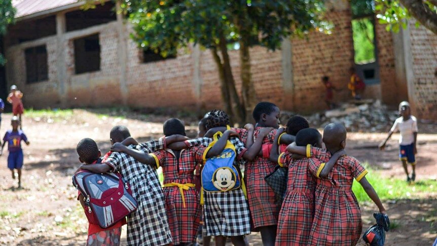 The back of a group of eight school children walking together while embracing.