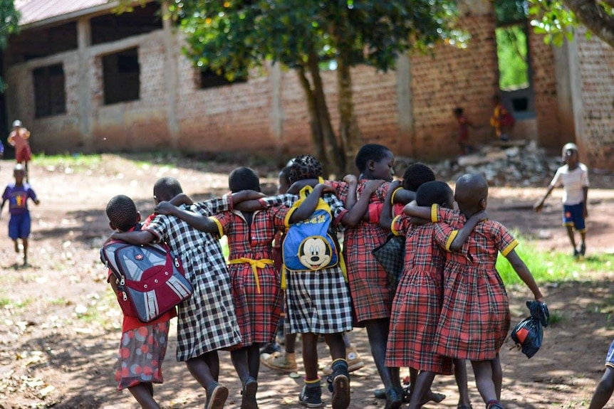 The back of a group of eight school children walking together while embracing.