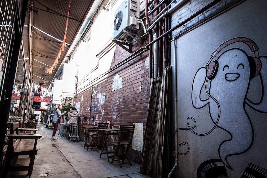 Looking down a narrow laneway with tables and chairs set out and art on the walls.