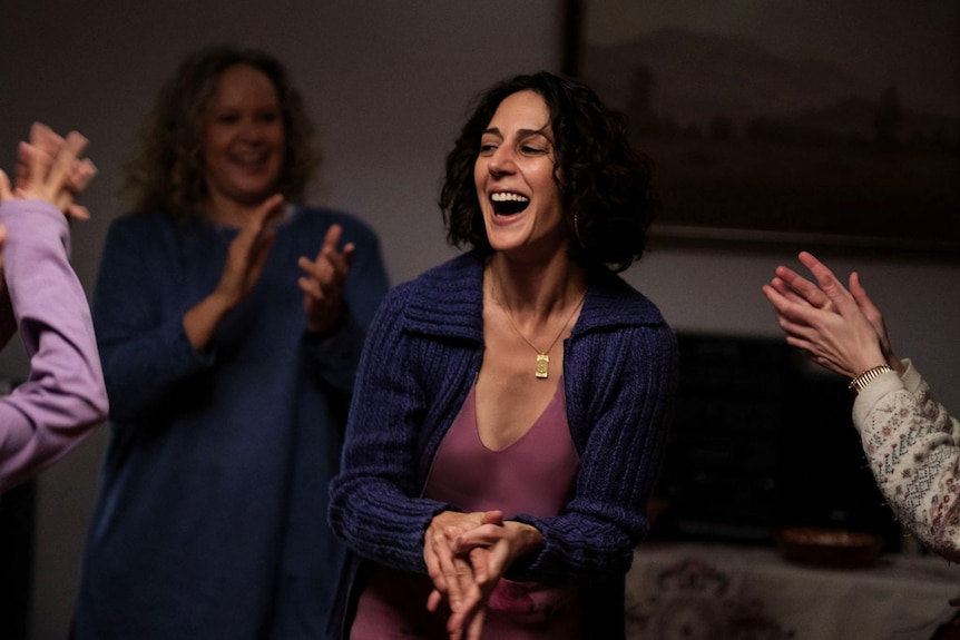 A woman smiles and claps her hands among a group of women, also clapping.