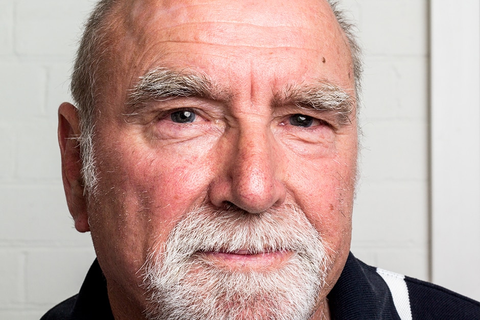 An older man in front of a white wall.