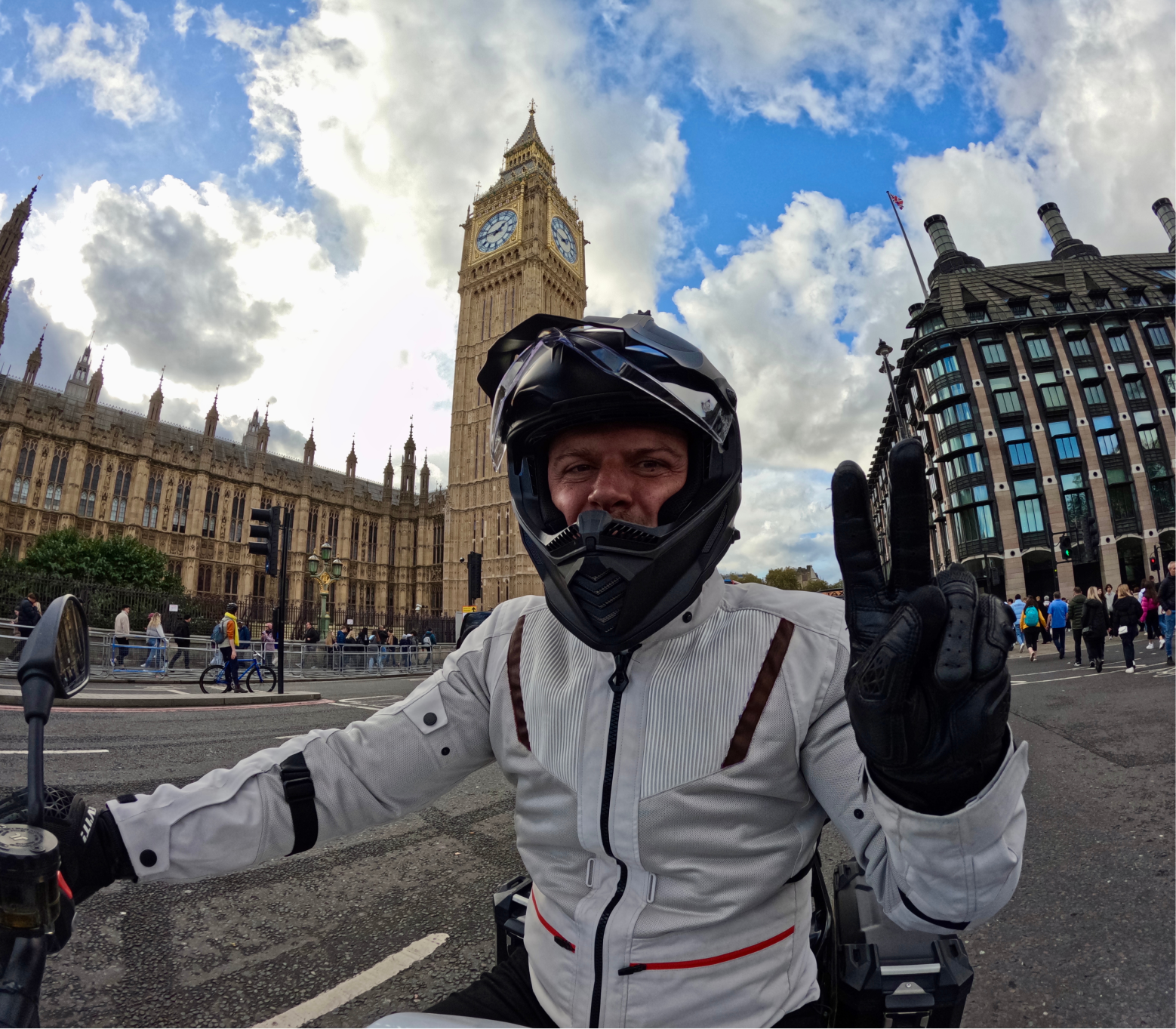 A man poses on a motorcycle in front of an old clock tower in a city