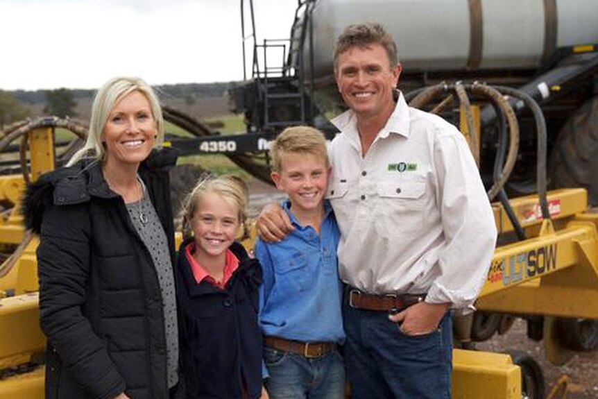 A woman and man stand with their two children in front of a piece of machinery.