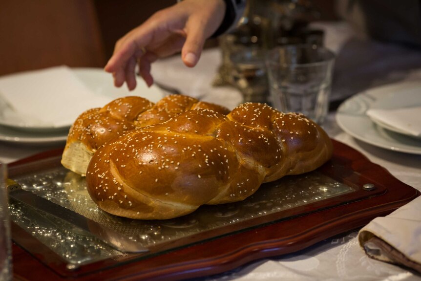 Two loaves of challah bread are laid in the centre of a table set for Shabbat in the home of Rabbi Pesach Steinberg.