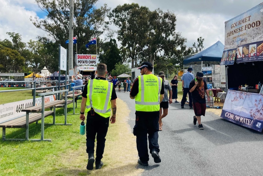 Two men in bright yellow vests walk through the grounds at a showground.