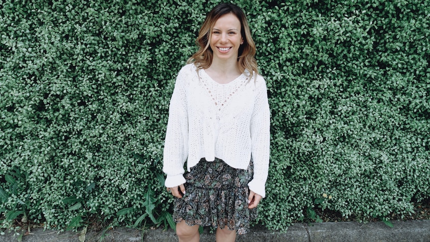 Lena Moxon smiles while standing in front of a wall of green plants.