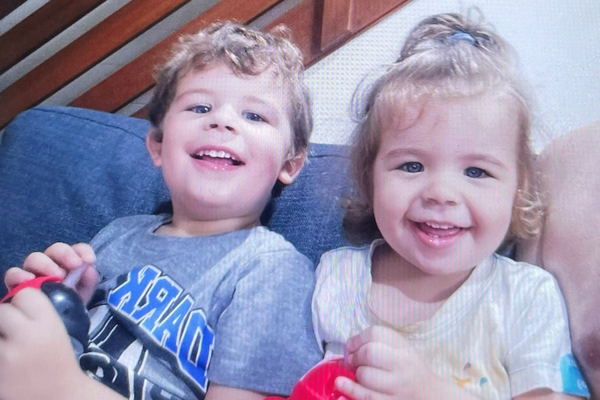 Two children, a young boy and a girl, sitting next to each other on a couch. 