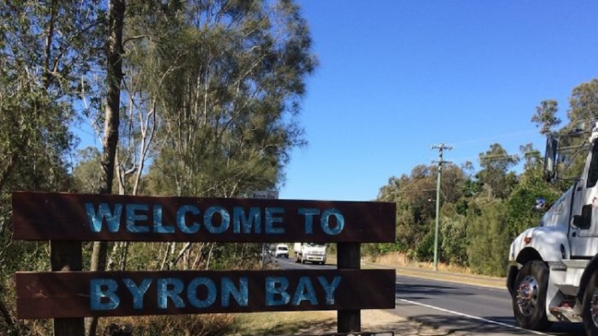 A welcome to Byron Bay sign with a car driving past