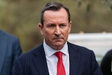 A close up of Mark McGowan wearing a blue suit and red tie, with a stern expression on his face.
