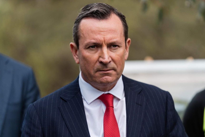 A close up of Mark McGowan wearing a blue suit and red tie, with a stern expression on his face.