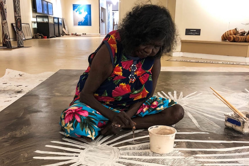 An Indigenous artist in the midst of painting.