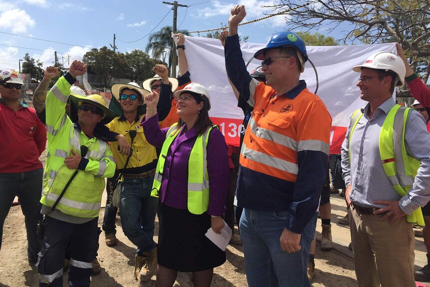 Building workers and Employment Minister Grace Grace raise a flag on a Brisbane work site