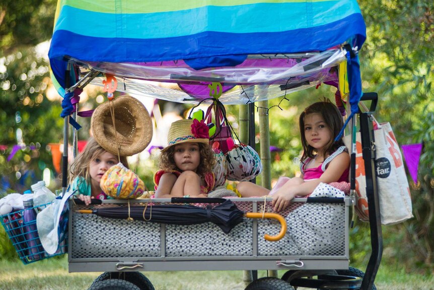 Three young children sitting in a colourful cart at Woodford Folk Festival, in Queensland.