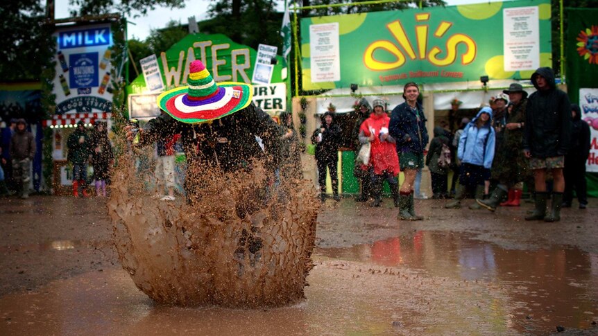 A festival-goer jumps in a puddle at Glastonbury.