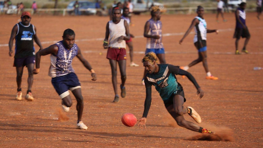 Footballers play in red dirt.