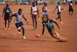 Footballers play in red dirt.